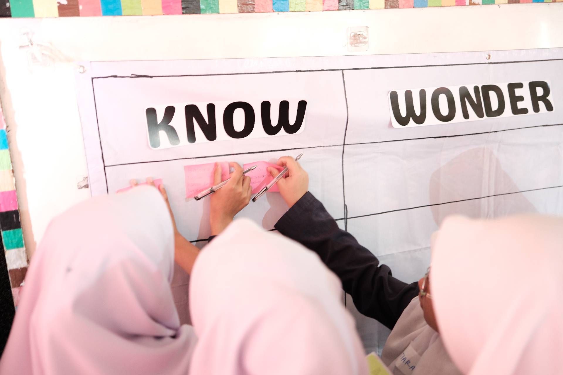 Siswi menempelkan sticky note di papan KWL